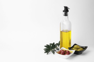 Photo of Bottle of cooking oil, olives and leaves on white background. Space for text