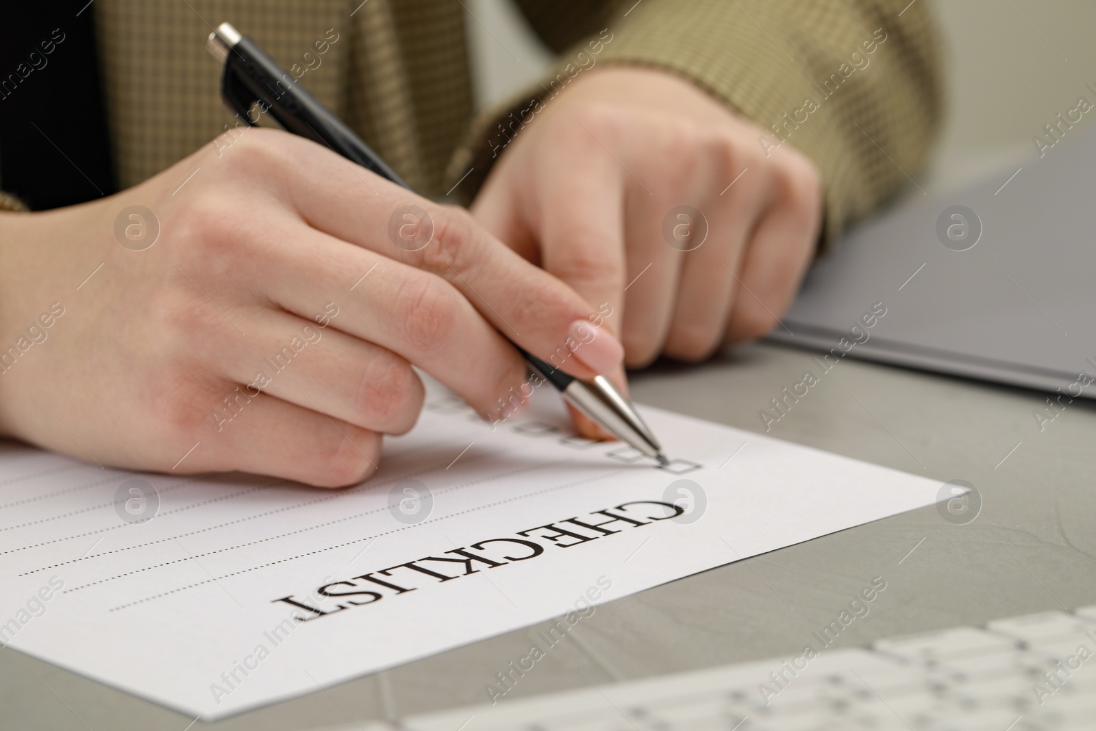 Photo of Woman filling Checklist at light grey table, closeup