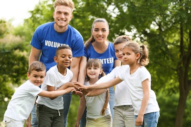 Group of kids joining hands with volunteers in park