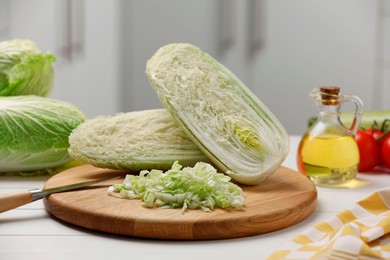 Photo of Fresh Chinese cabbages, knife and oil on white wooden table in kitchen