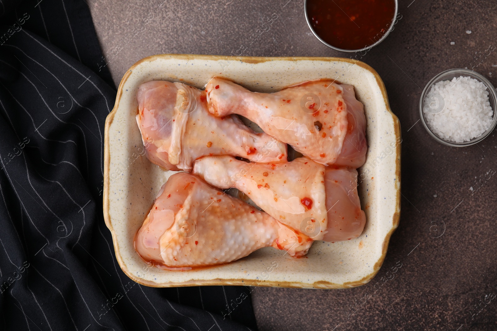 Photo of Fresh marinade, raw chicken drumsticks and salt on brown table, flat lay