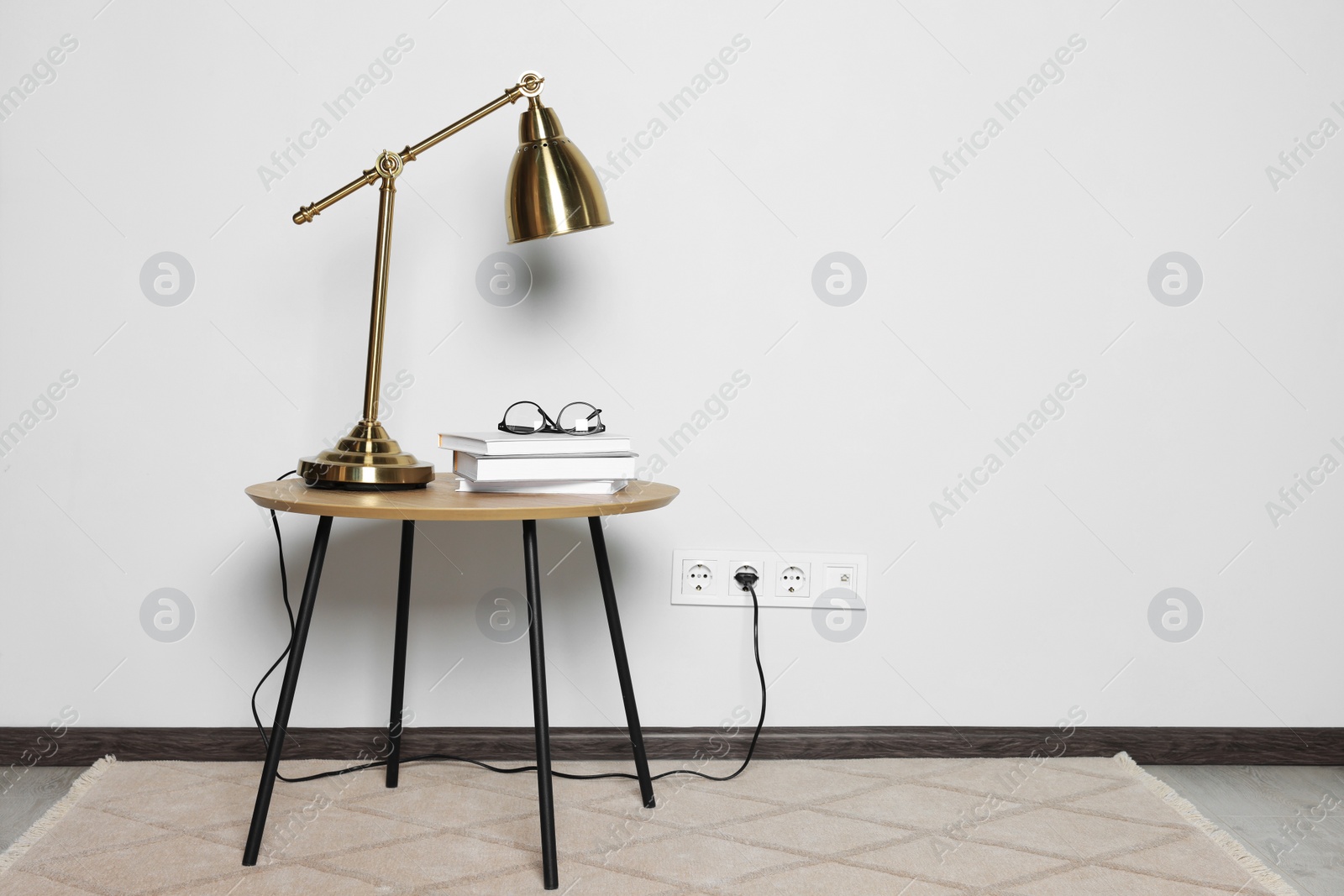 Photo of Lamp with books on wooden table near white wall, space for text