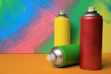 Cans of different spray paints on color background, space for text. Graffiti supplies