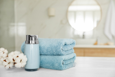 Clean towels, cotton flowers and soap dispenser on white wooden table in bathroom