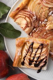 Tasty apple pie with chocolate topping, fresh fruits and green leaves on table, flat lay