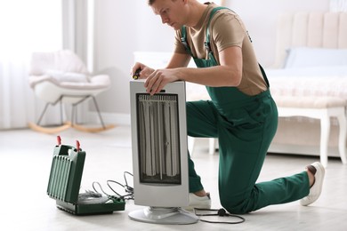 Photo of Professional technician repairing electric ultrared heater with screwdriver indoors