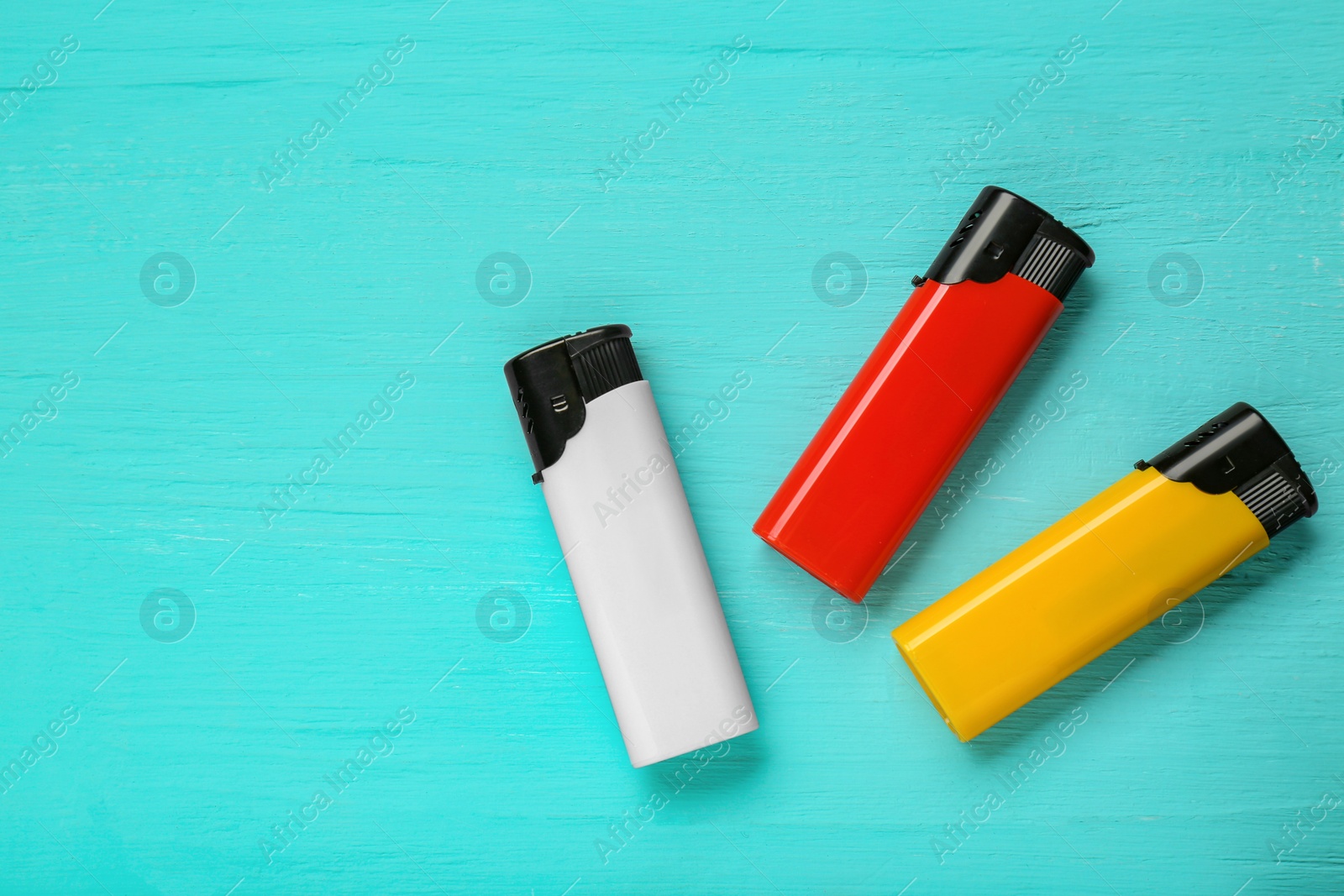 Photo of Stylish small pocket lighters on turquoise wooden background, flat lay. Space for text