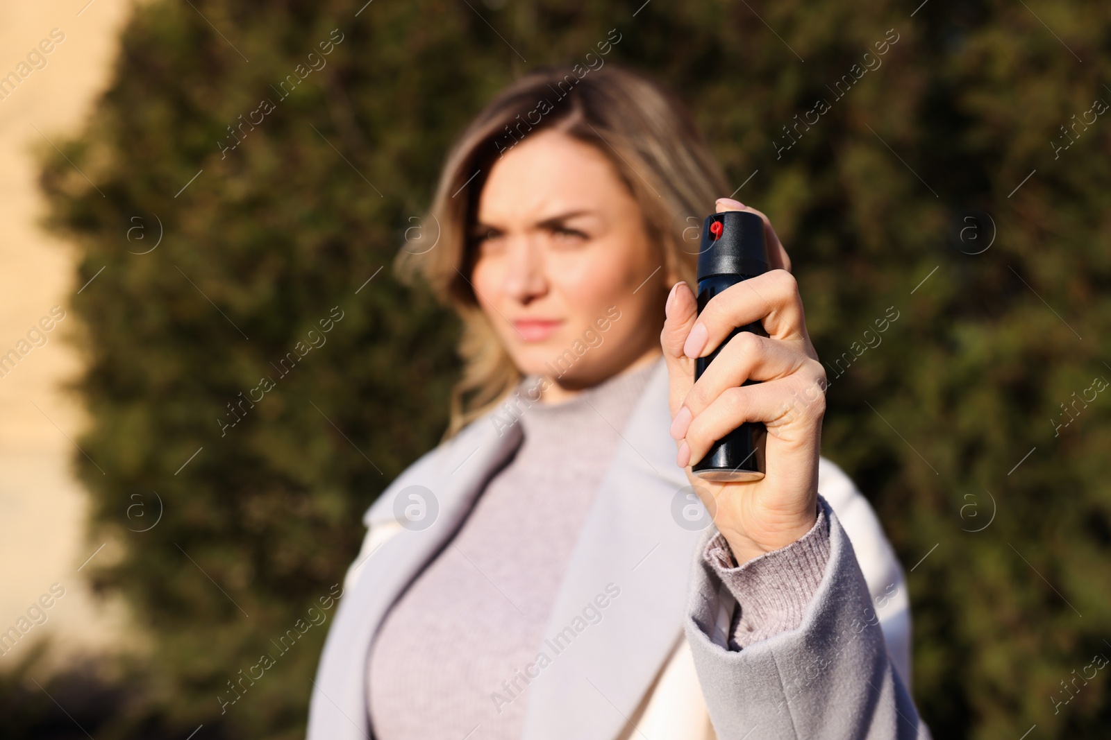 Photo of Young woman using pepper spray outdoors, focus on hand