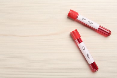 Photo of Tubes with blood samples and labels STD Test on white wooden table, flat lay. Space for text