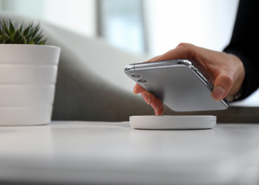 Photo of Woman putting smartphone on wireless charger in room, closeup. Space for text