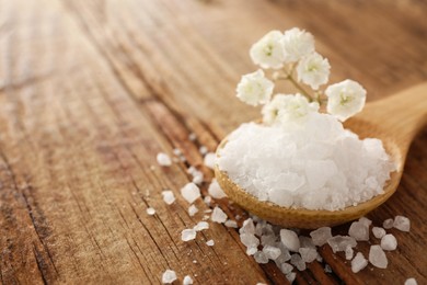 Photo of Aromatic sea salt and beautiful flowers on wooden table, closeup. Space for text
