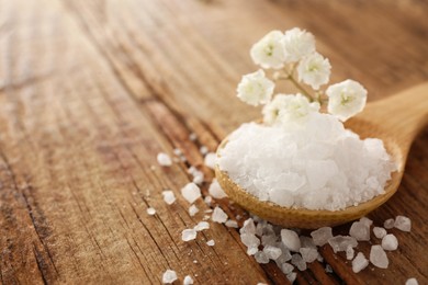 Aromatic sea salt and beautiful flowers on wooden table, closeup. Space for text