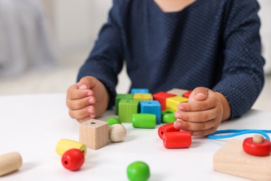 Motor skills development. Little girl playing with wooden pieces and string for threading activity at table, closeup