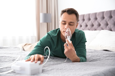 Photo of Young man with asthma machine on bed in light room