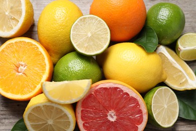 Photo of Different fresh citrus fruits and leaves on wooden table, above view