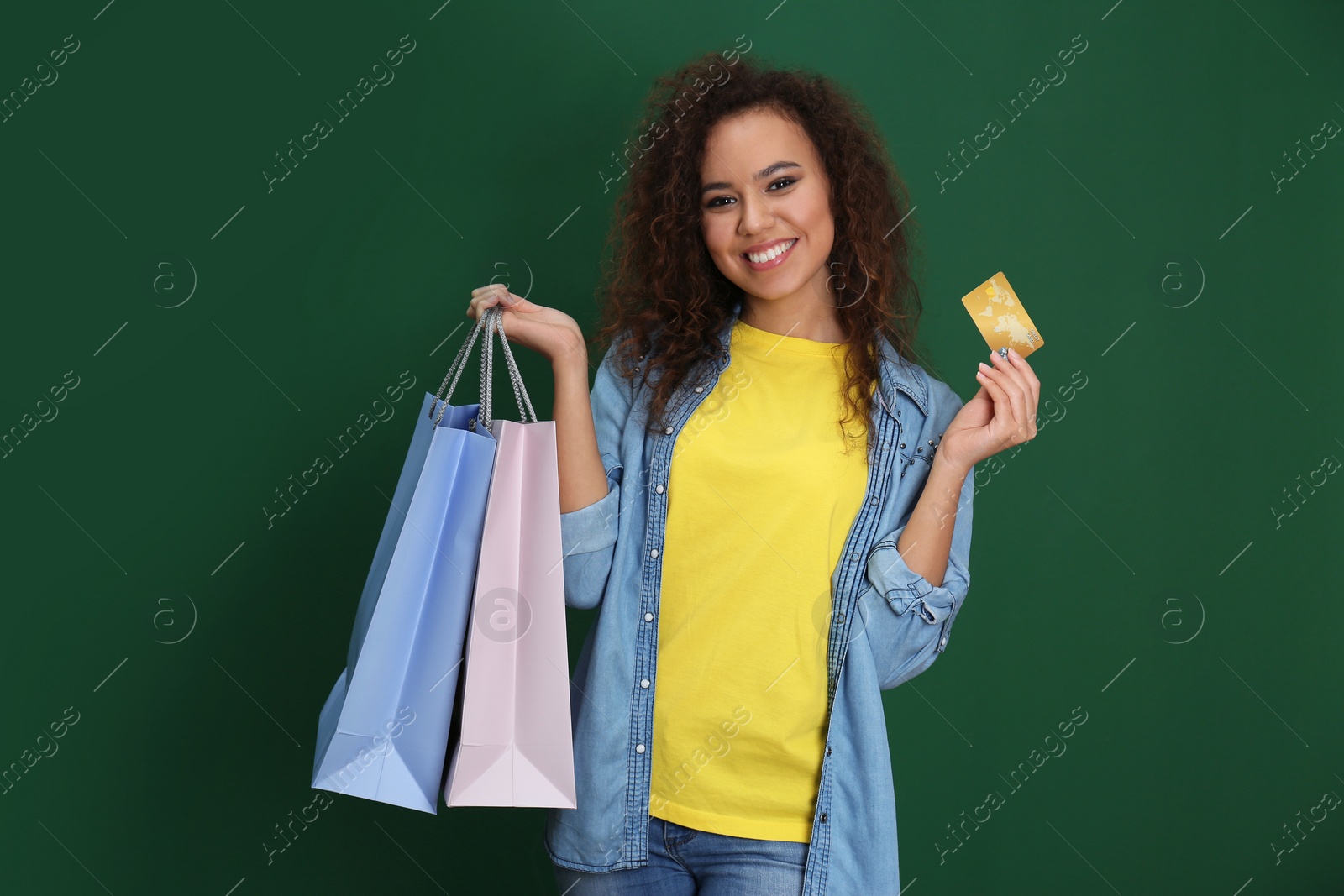 Photo of Young African-American woman with credit card and shopping bags on color background. Spending money