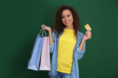 Photo of Young African-American woman with credit card and shopping bags on color background. Spending money