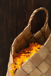 Photo of Beautiful calendula flowers in wicker bag against wooden wall