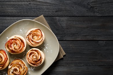 Photo of Freshly baked apple roses on dark wooden table, top view. Space for text