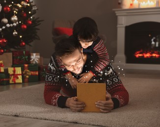Image of Father and his cute son opening gift box with magical light on floor at home. Christmas celebration