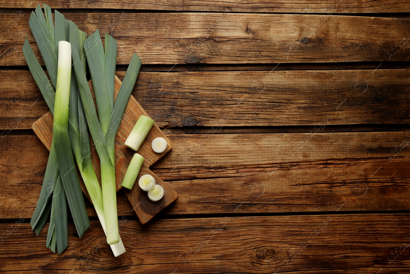 Photo of Fresh raw leeks on wooden table, top view. Space for text.