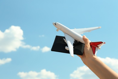 Woman holding toy airplane and passport against blue sky, closeup