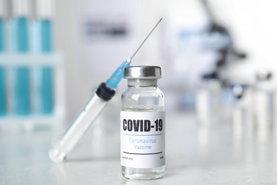 Vial with vaccine against Covid-19 and syringe on white table indoors