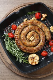 Photo of Delicious homemade sausage with garlic, tomatoes, rosemary and spices in grill pan on wooden table, top view