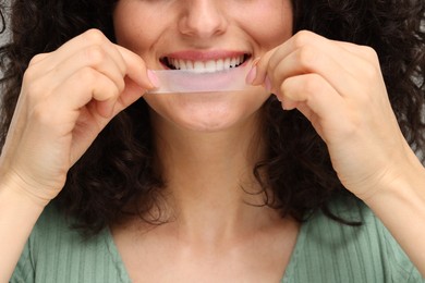 Photo of Young woman applying whitening strip on her teeth, closeup