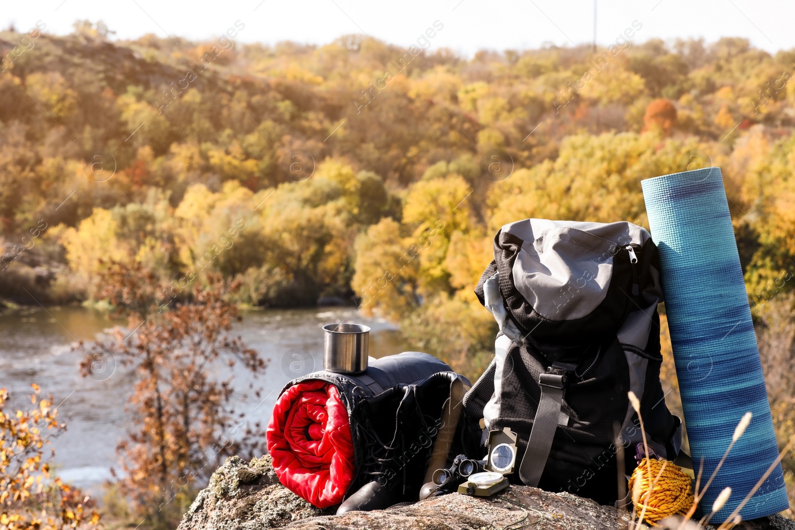 Photo of Set of camping equipment with sleeping bag on rock outdoors. Space for text