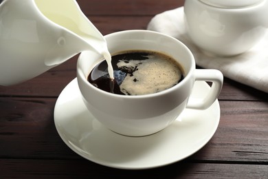 Pouring milk into cup of hot coffee on wooden table