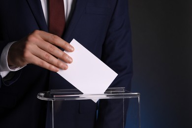 Photo of Man putting his vote into ballot box on dark background, closeup. Space for text