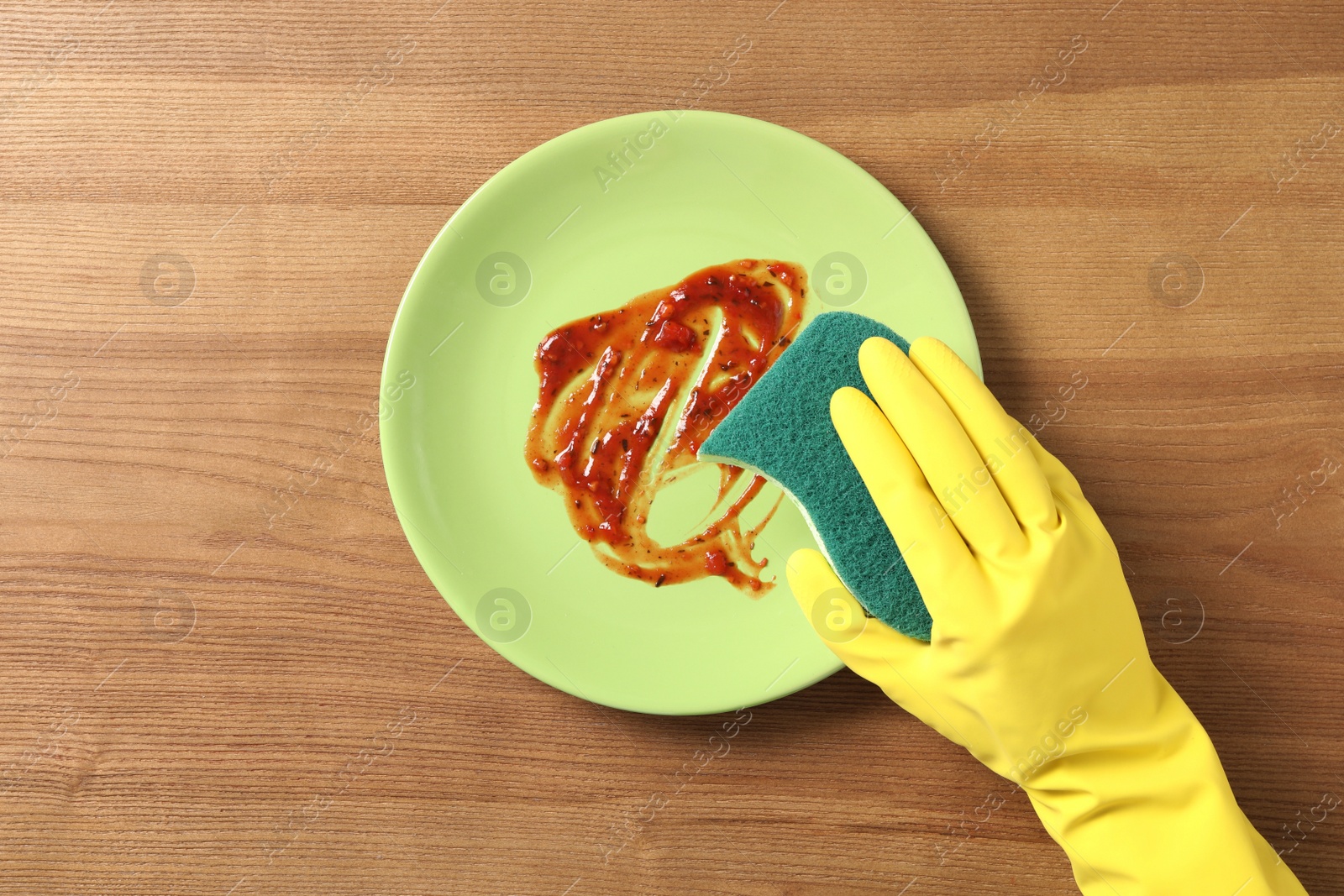 Photo of Woman washing dirty plate at wooden table, top view