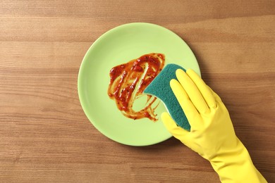 Woman washing dirty plate at wooden table, top view