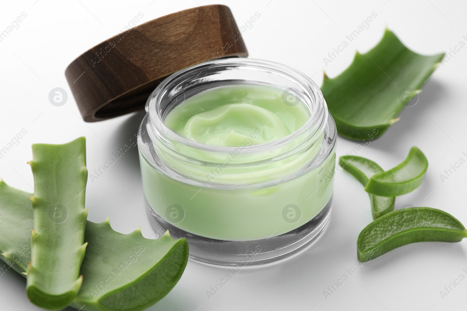 Photo of Jar of natural cream and aloe leaves on white background, closeup