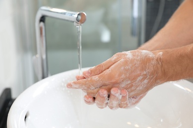 Photo of Man washing hands with soap over sink in bathroom, closeup