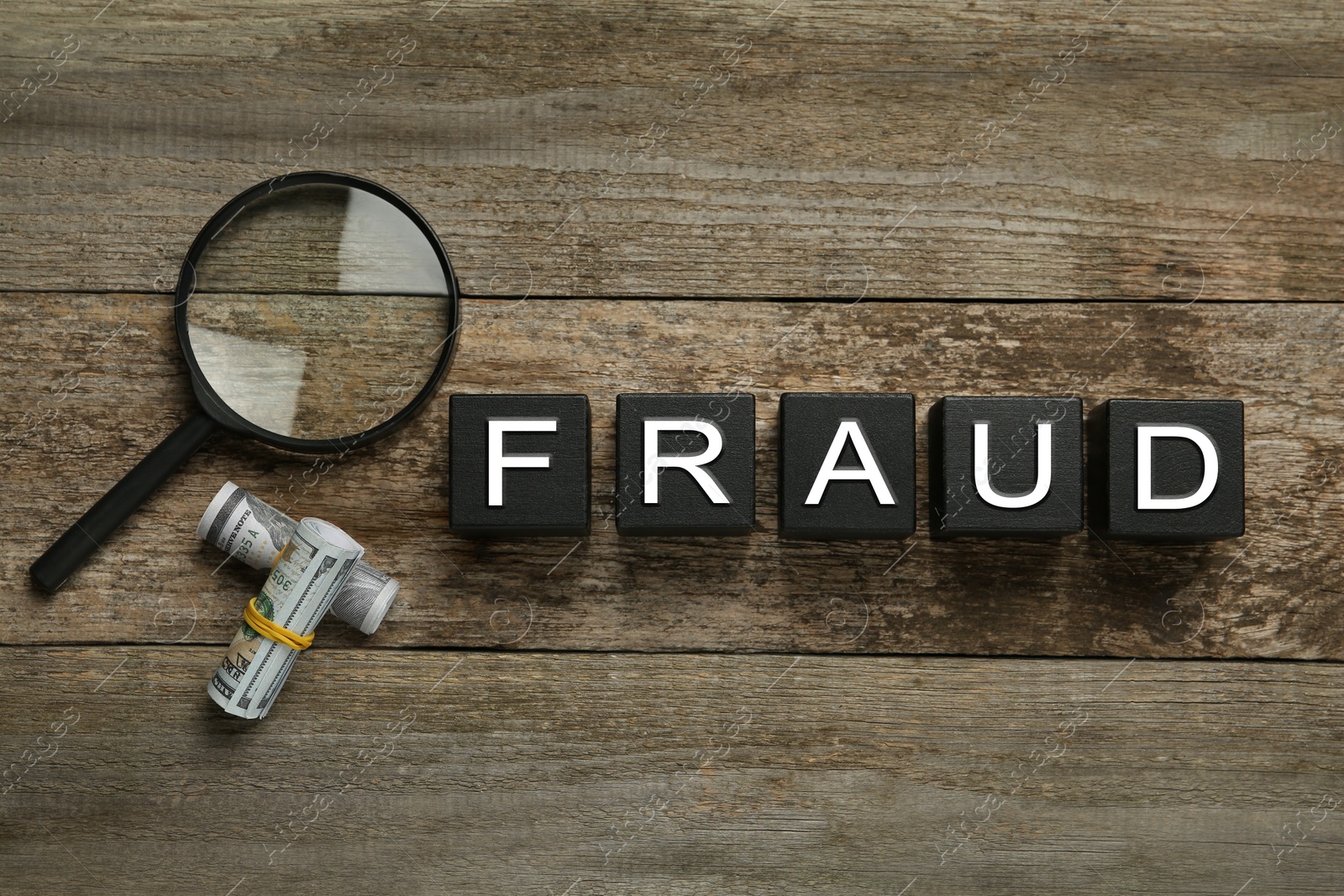 Photo of Black cubes with word Fraud, magnifying glass and dollar banknotes on wooden table, flat lay