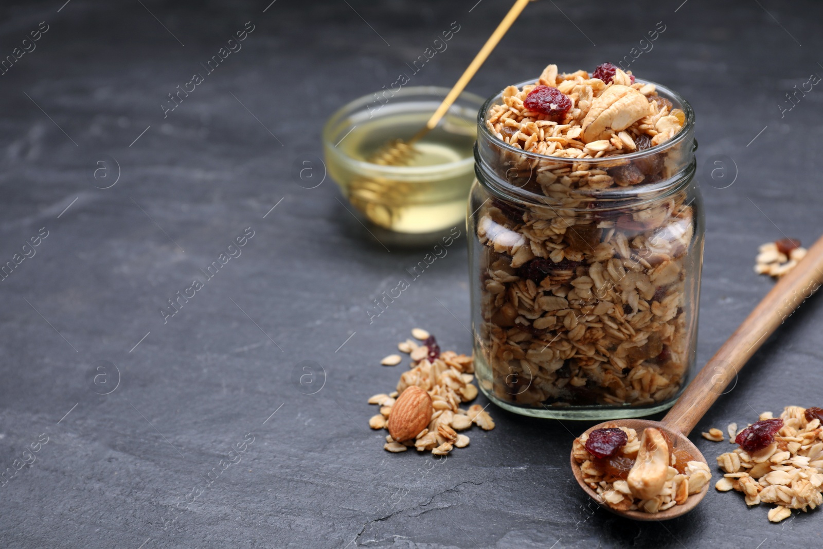 Photo of Jar of tasty granola with nuts and dry fruits on black table. Space for text