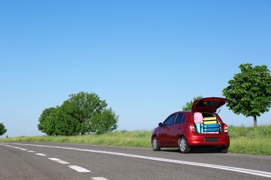 Photo of Family car with open trunk full of luggage on highway. Space for text