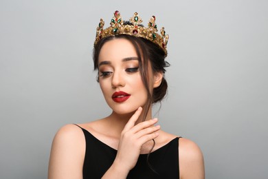 Beautiful young woman wearing luxurious crown on light grey background