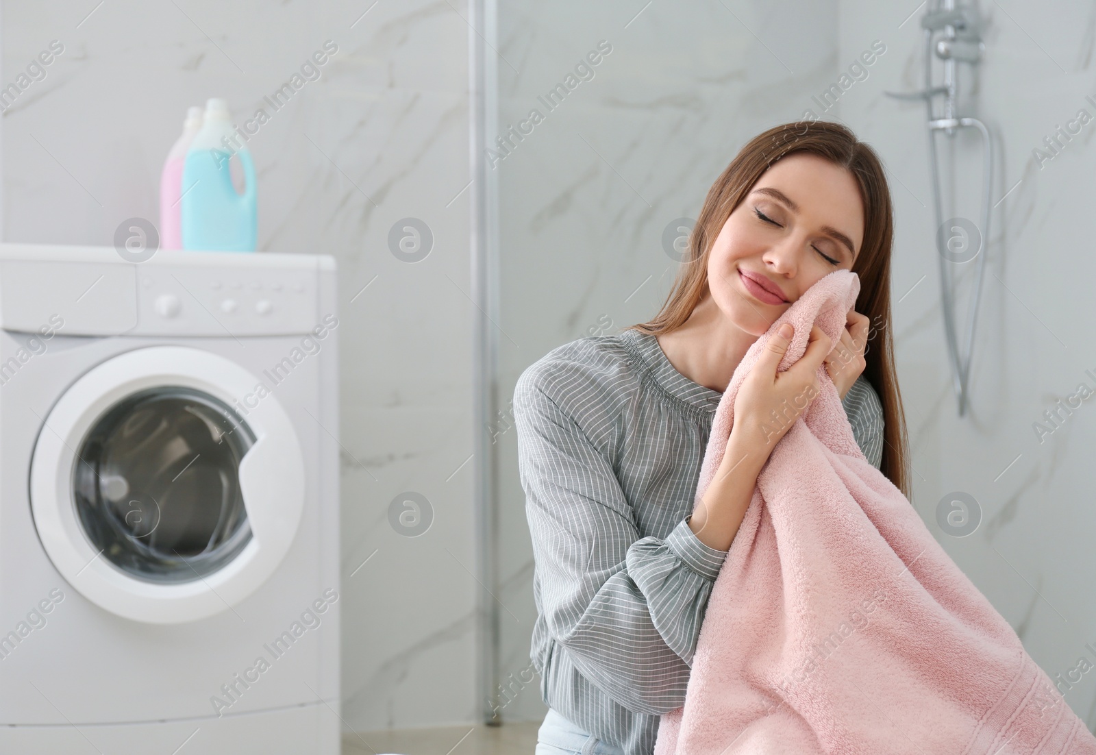 Photo of Happy woman with clean towel near washing machine in bathroom. Laundry day