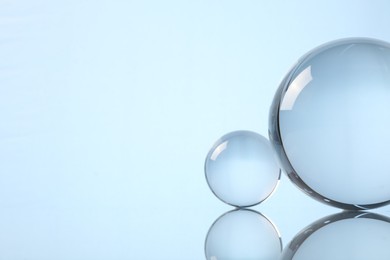Photo of Transparent glass balls on mirror surface against light background. Space for text