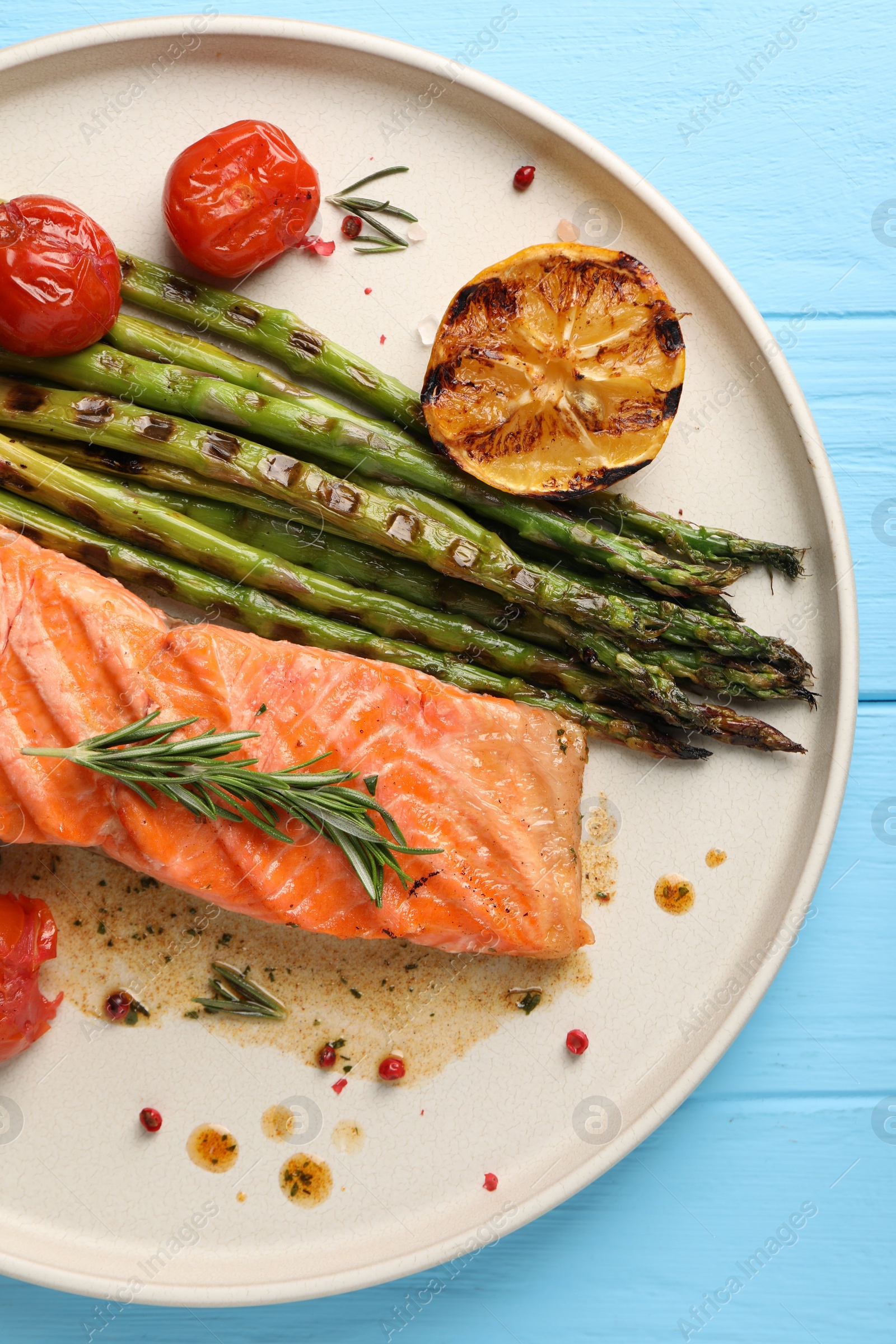 Photo of Tasty grilled salmon with tomatoes, asparagus and spices on light blue table, top view