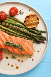 Tasty grilled salmon with tomatoes, asparagus and spices on light blue table, top view