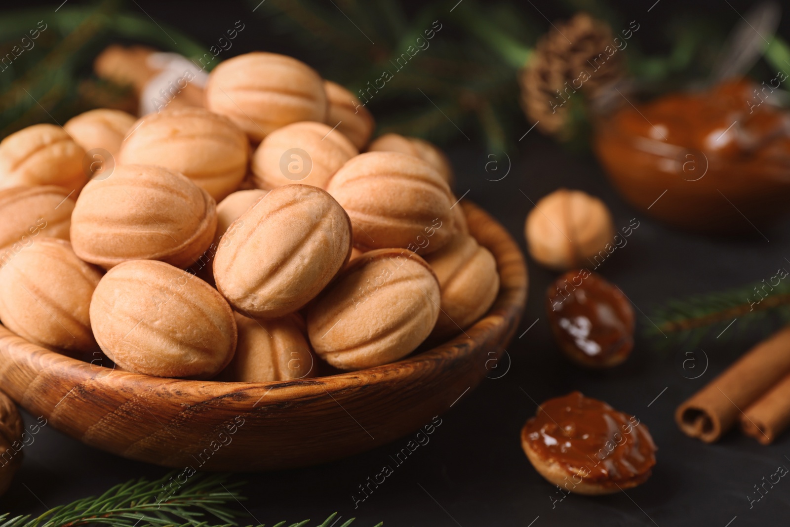 Photo of Homemade walnut shaped cookies with boiled condensed milk, cinnamon sticks and fir branches on black table, closeup