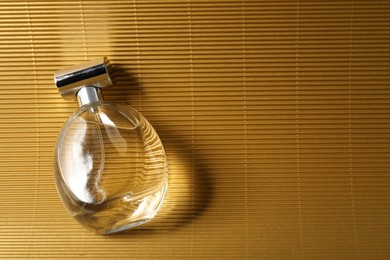 Photo of Luxury women's perfume. Sunlit glass bottle on golden surface, top view. Space for text