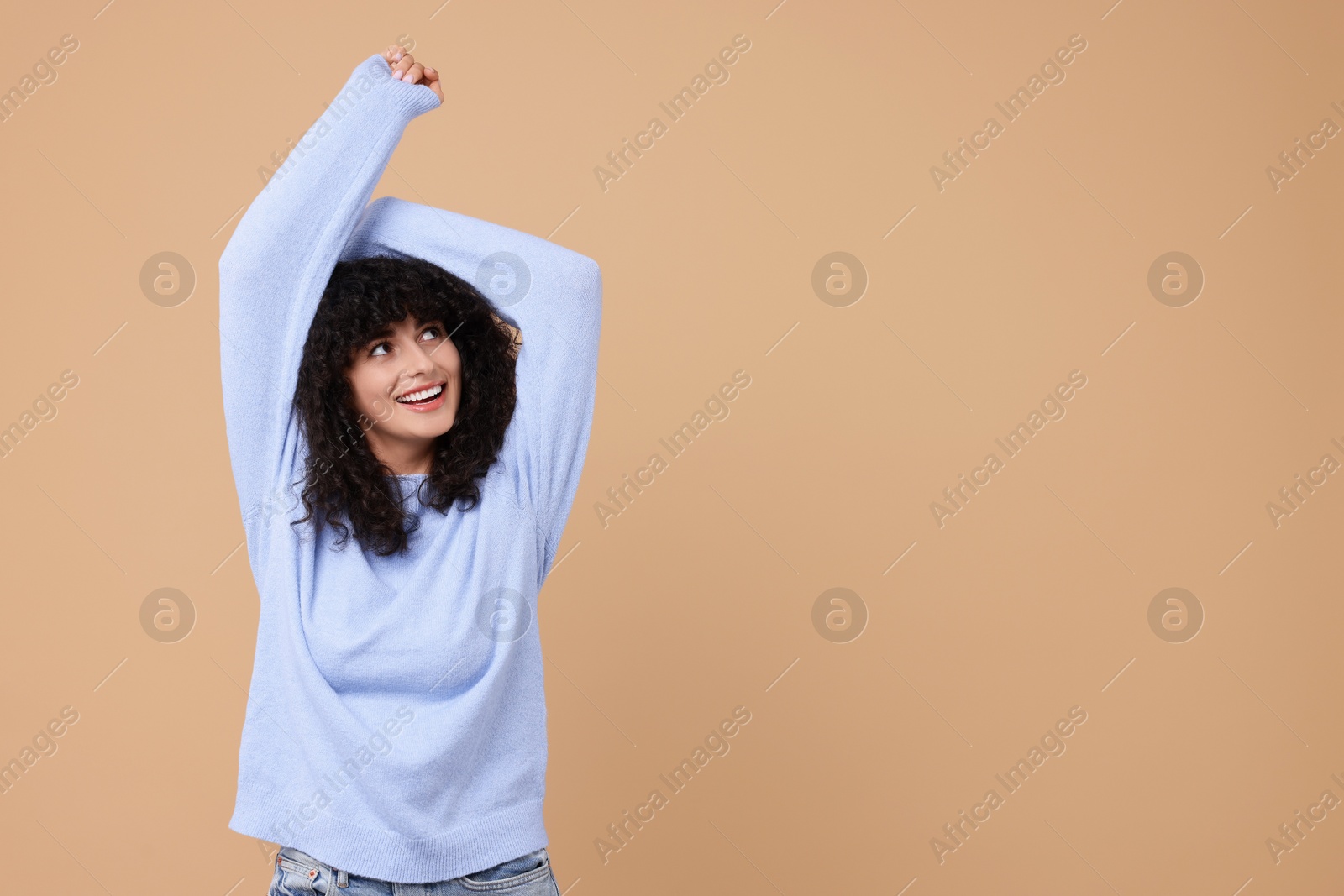 Photo of Happy young woman in stylish light blue sweater on beige background, space for text
