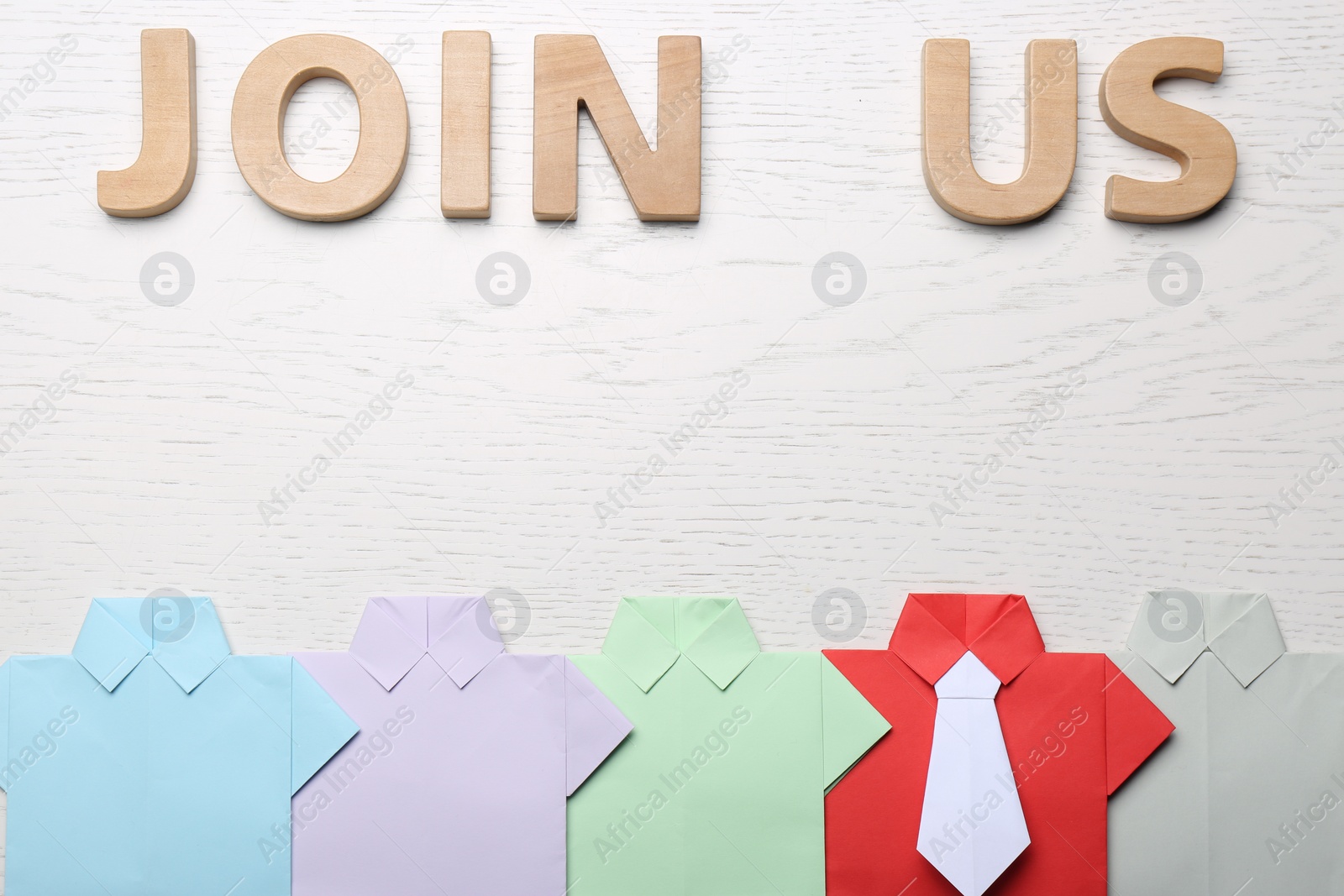 Photo of Many paper shirts and phrase Join Us on white wooden background, flat lay. Recruiter searching employee