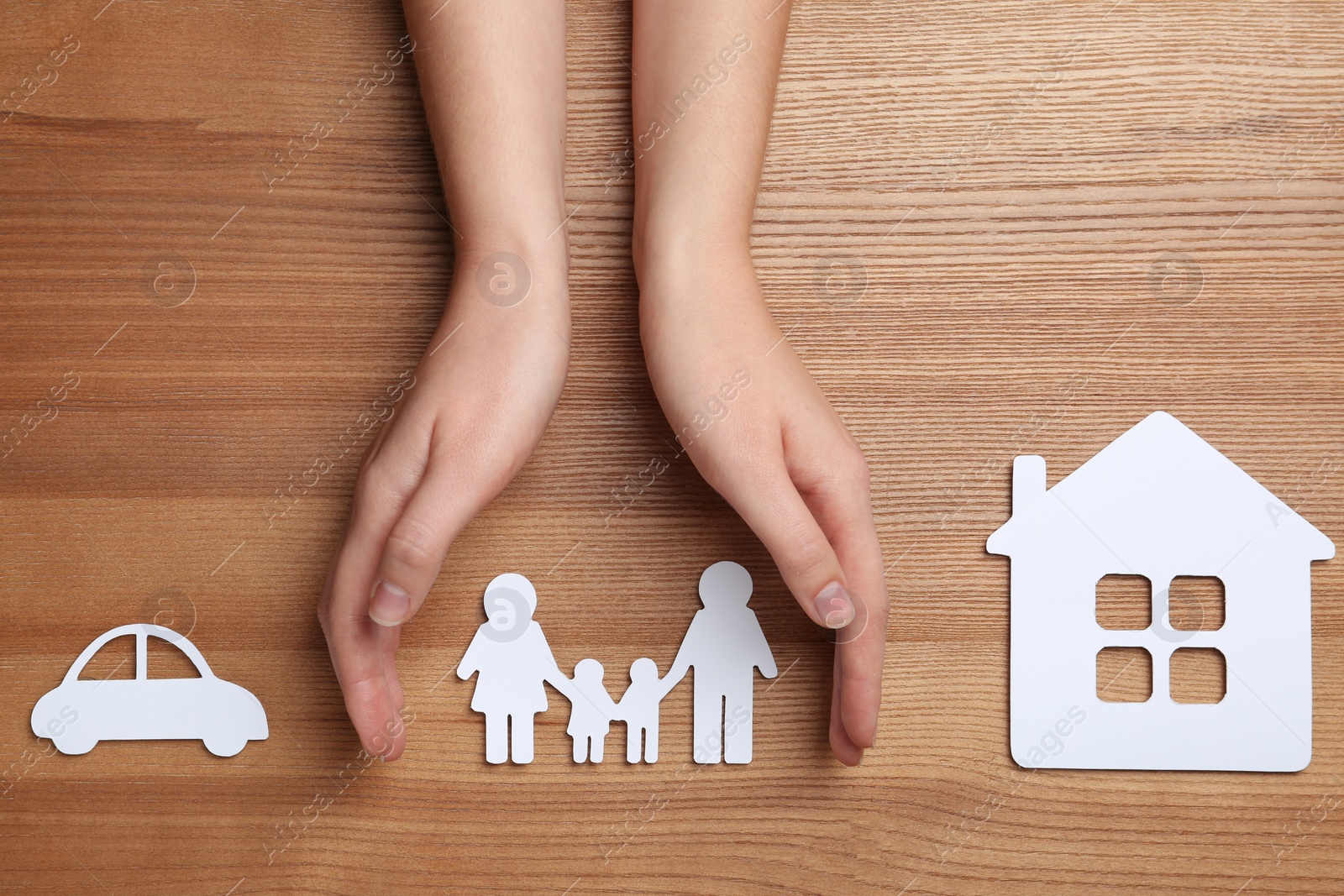 Photo of Woman holding hands over paper silhouette of family on wooden background, top view. Life insurance concept