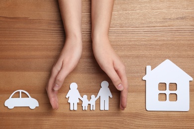 Photo of Woman holding hands over paper silhouette of family on wooden background, top view. Life insurance concept